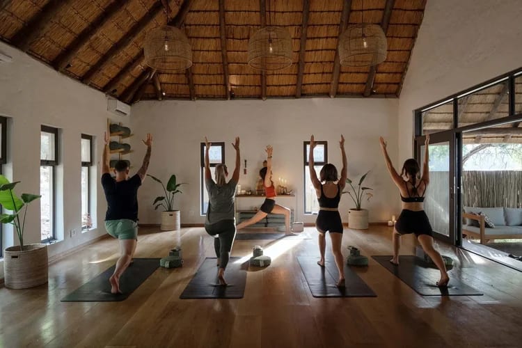 Guests holding a yoga pose in a light-filled thatched studio with timber floors and garden views